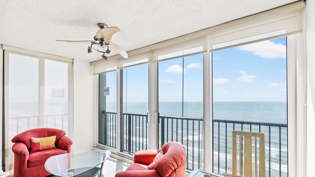 A balcony with a glass table and two red chairs, overlooking the ocean. - ~ Beach Breeze ~   Beautiful Oceanfront 3 Bed/2 Bath Condo (Myrtle Beach)