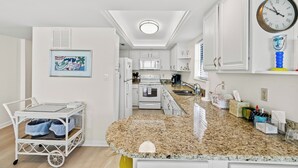 A modern kitchen with white cabinets, a granite countertop, and a clock on the wall. - ~ Beach Breeze ~   Beautiful Oceanfront 3 Bed/2 Bath Condo (Myrtle Beach)