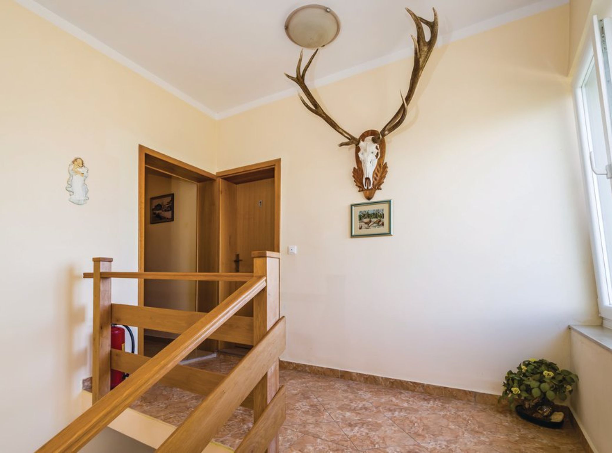 A staircase with wooden railings leading to an upper floor, a wall-mounted deer skull, and a framed picture.