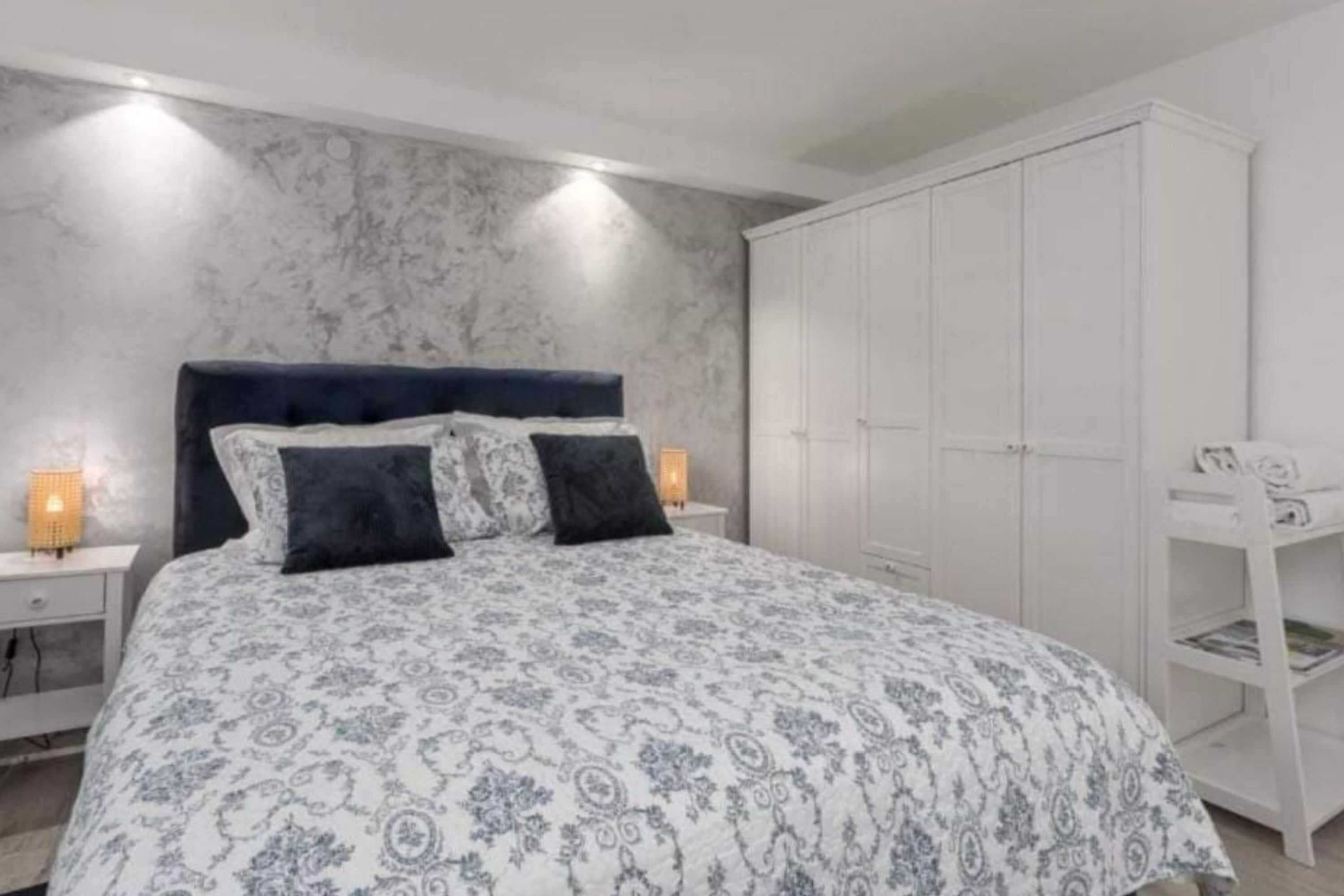 A bedroom with a bed, nightstands, a wardrobe, and a desk with a lamp.
