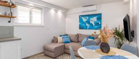 Una sala moderna con un sofá seccional, una mesa de comedor con sillas, una zona de cocina con encimera y estanterías, y una gran obra de arte con un mapa del mundo en la pared.