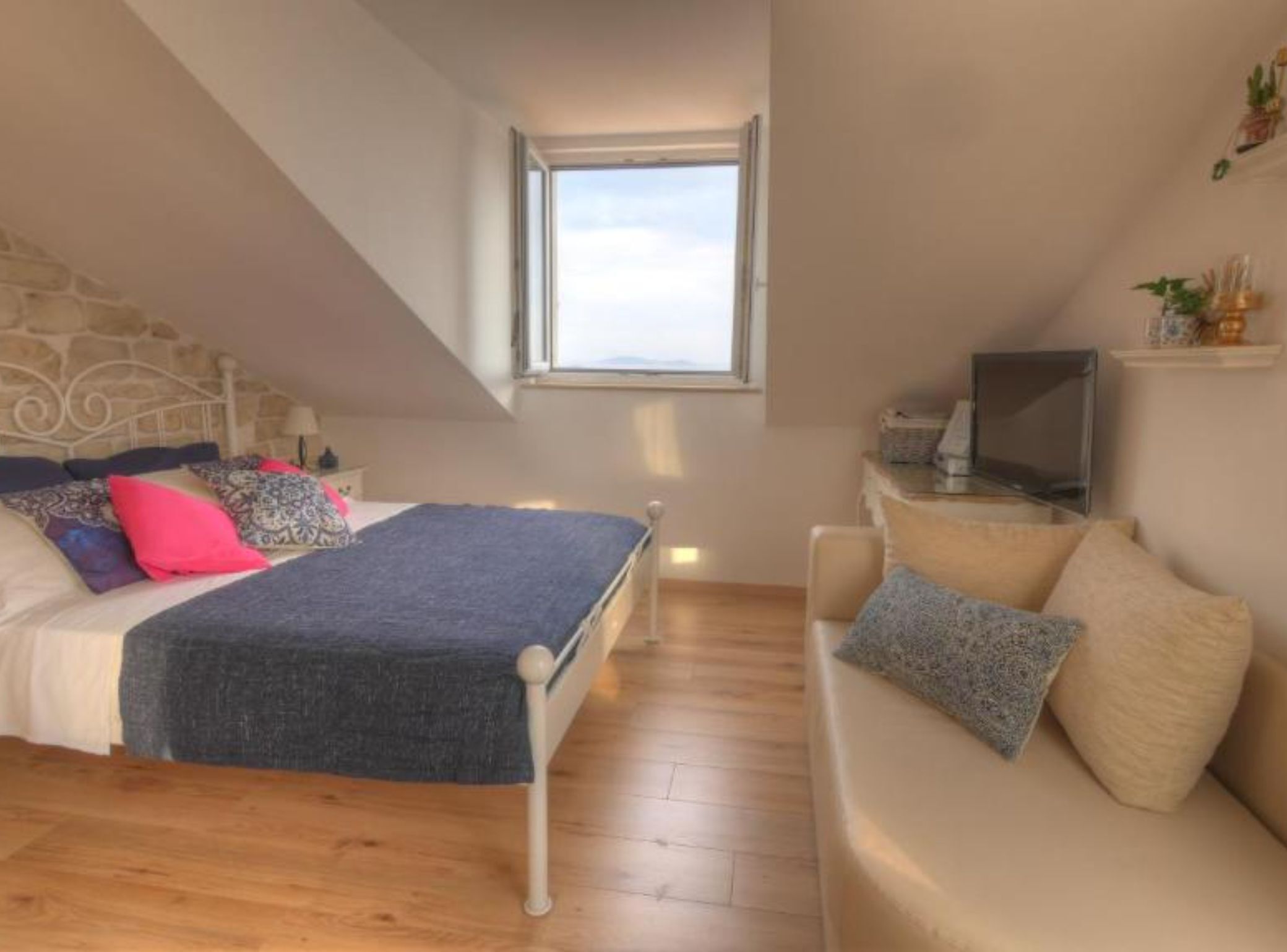 A bedroom with a bed, a TV, a sofa, and a window.