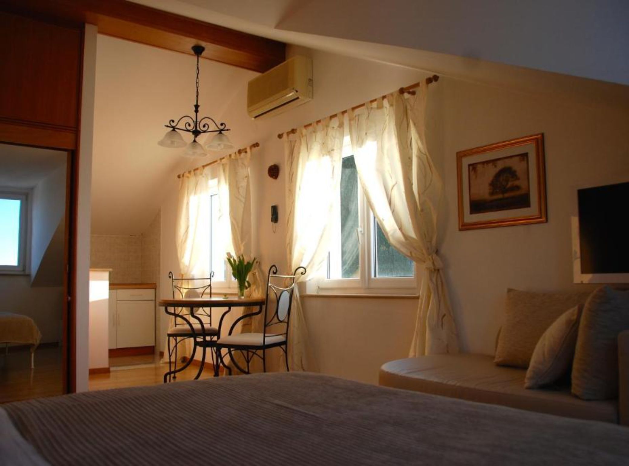 A cozy bedroom with a bed, a dining table with chairs, a sofa, and a window with curtains.