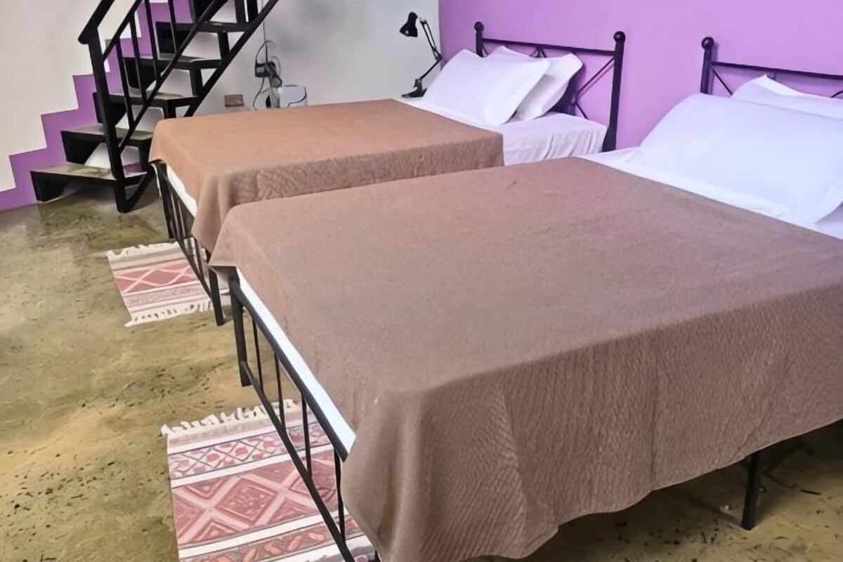 Two single beds with brown covers, a staircase, and a purple wall.