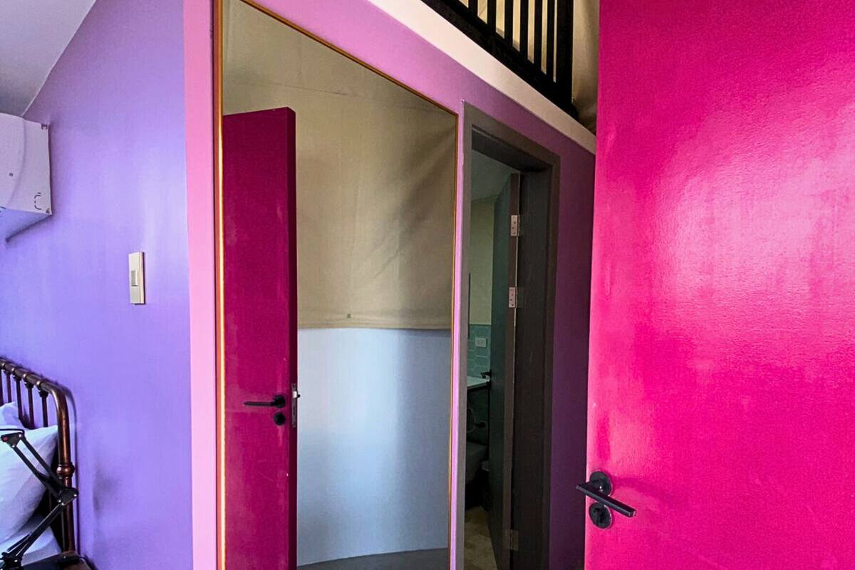 Ett rum med en rosa dörr, en säng och ett skrivbord med en lampa.