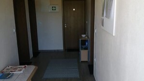 Um corredor com porta de madeira, uma mesinha com revistas e um tapete estampado.