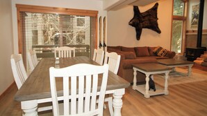 A dining area with a wooden table and white chairs, a brown sofa, and a mounted animal head on the wall. - Tamarack #39: 2  BR, 2.5  BA Condominium in Mammoth Lakes, Sleeps 8 (Mammoth Lakes)