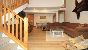 A spacious living area with a wooden staircase, a large brown sofa, a dining table, and a mounted animal head on the wall. - Tamarack #39: 2  BR, 2.5  BA Condominium in Mammoth Lakes, Sleeps 8 (Mammoth Lakes)