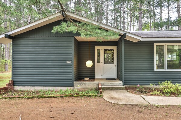 A single-story house with a dark exterior, a white front door, and a small porch area.