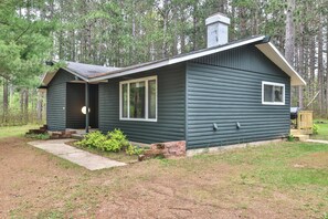 A small, dark green cabin with a porch, a chimney, and a deck.