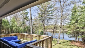 A deck with blue cushioned seating overlooking a lake surrounded by trees.