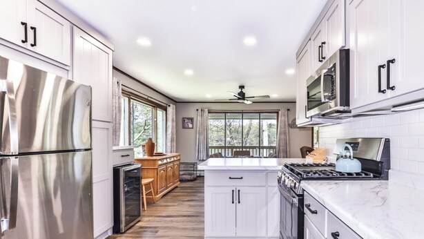 A modern kitchen with stainless steel appliances, white cabinetry, and a large window providing natural light.