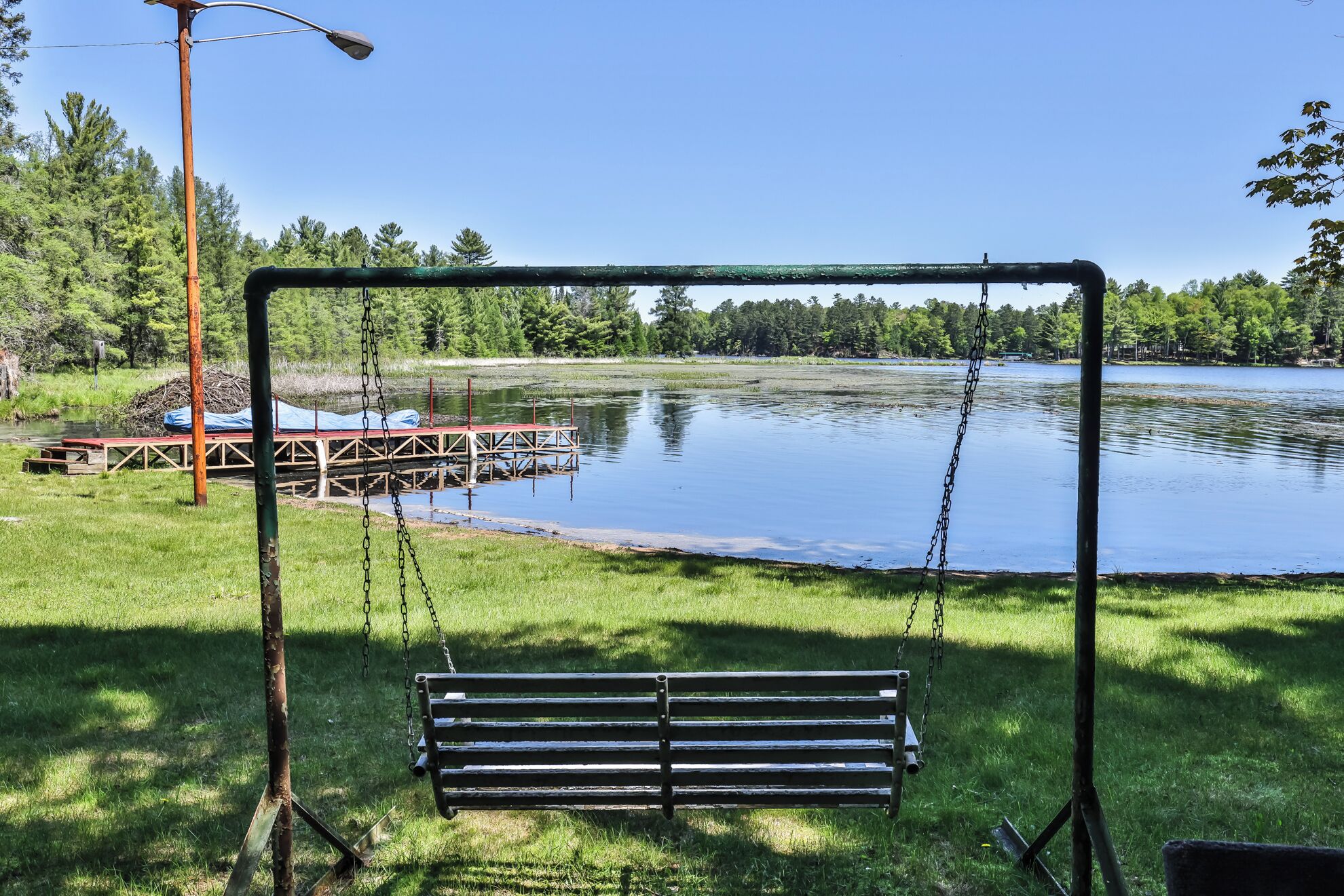 Eine Schaukel im Park, im Hintergrund ein See und eine Anlegestelle.