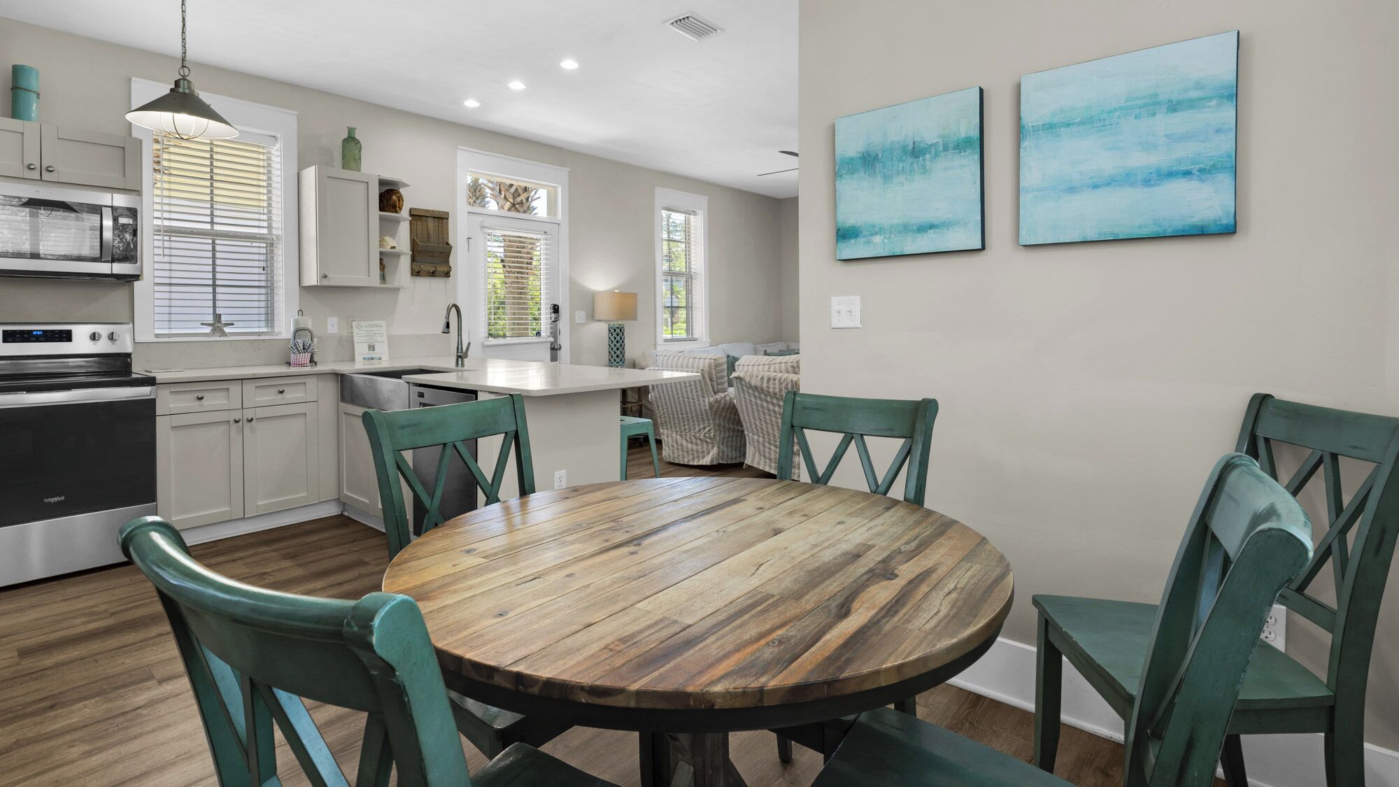 A modern kitchen with white cabinets, a stainless steel stove, and a dining area with a wooden table and green chairs.