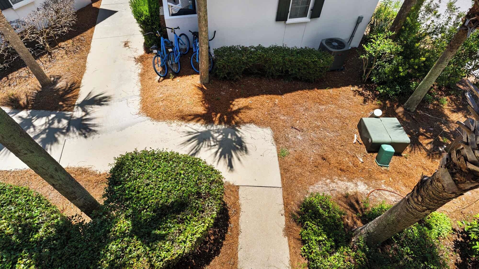 A residential property with a paved driveway, a blue bicycle, a small green outdoor seating area, and a white building with a window and a door.