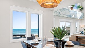 A dining area with a view of the ocean, a wooden table set with plates and glasses, and a potted plant. - Wavesong: Brand New Build, Beachfront, Private Pool, Pet Friendly, East End (St. George Island)