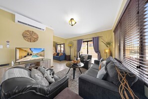 A living room with a sofa, a coffee table, and a television displaying a pool view.