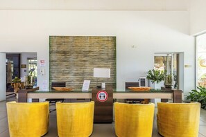 A reception area with a glass desk, a sign indicating a waiting area, and yellow chairs.