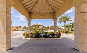 A covered entrance with a paved pathway leading to a building, palm trees, and a clear sky.