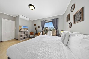 A bedroom with a large bed, a TV, a wardrobe, and a balcony with curtains.