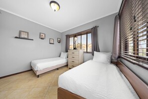 Een slaapkamer met twee bedden, een kaptafel en een raam met zonwering.