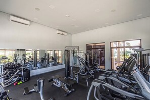 A gym with various exercise equipment, large windows, and an air conditioning unit.