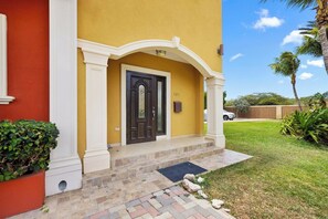 A yellow building with a black door, white columns, and a numbered address sign. - Stunning 3BR Oasis w Private Pool Patio near Beach (Noord)