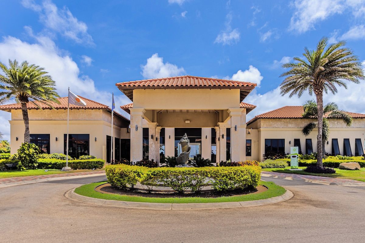 Entrada de un hotel con un arco central, palmeras y un jardín bien cuidado.
