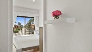 Une chambre d’hôtel avec un lit, une fenêtre avec des rideaux, un balcon avec une balustrade et un vase avec des fleurs accroché au mur.