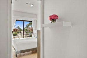 A hotel room with a bed, a window with curtains, a balcony with a railing, and a vase with flowers on the wall. - Private Pool & Backyard Oasis near Catalina Beach (Noord)