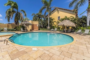 A swimming pool with lounge chairs and umbrellas, surrounded by palm trees and a building. - Private Pool & Backyard Oasis near Catalina Beach (Noord)