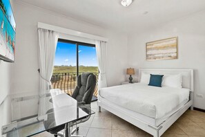 A hotel room with a bed, a desk, a chair, a window with a view, and a painting on the wall.