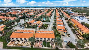 A coastal residential area with uniform orange-roofed houses, a central road, and a beach in the background.