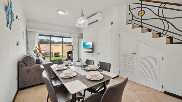 Un coin repas avec une table dressée pour quatre personnes, un canapé et un téléviseur fixé au mur.