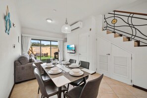 A dining area with a table set for four, a sofa, and a TV mounted on the wall.