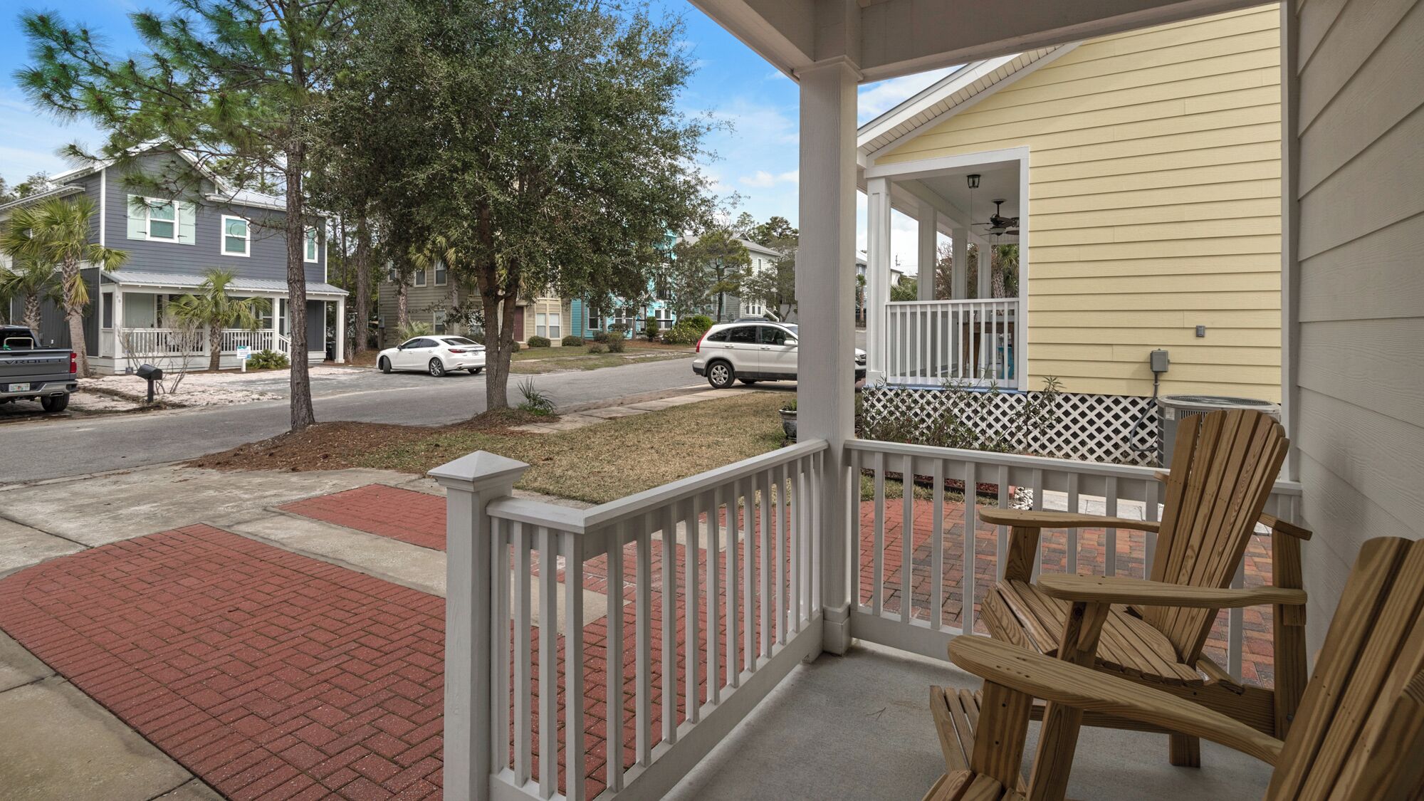 A porch with wooden chairs and a brick pathway leading to a street.