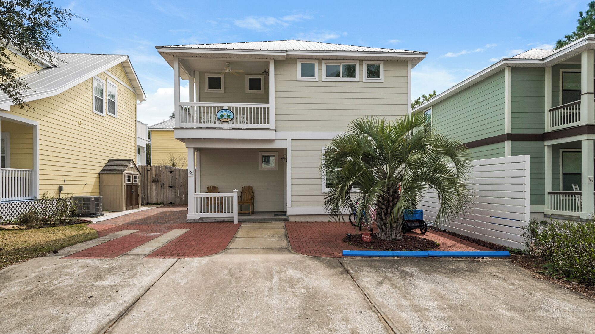 A two-story house with a balcony, a small porch, and a palm tree in the front yard.