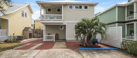 A two-story house with a balcony, a small porch, and a palm tree in the front yard.