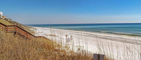 A beach with a wooden staircase leading down to the shore, a sandy beach, and the ocean.