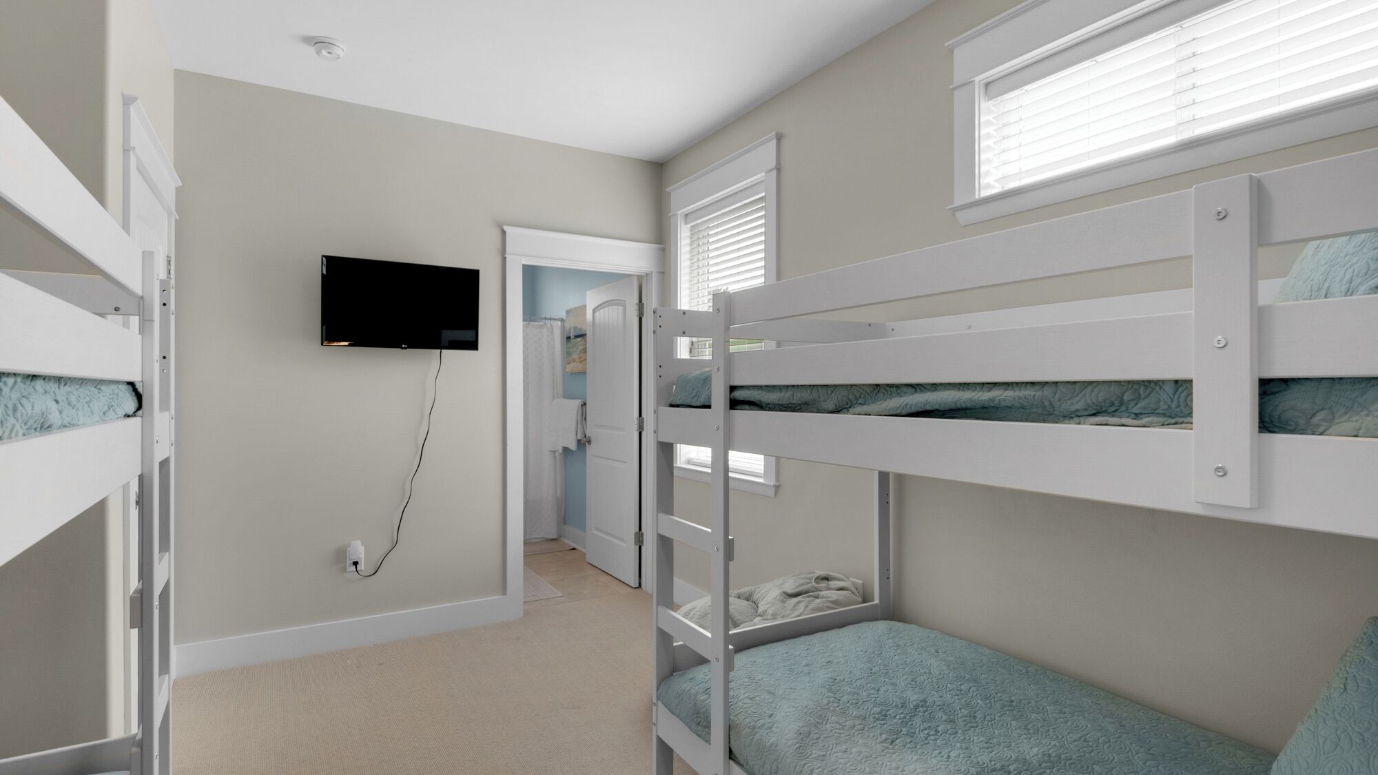 A bedroom with bunk beds, a television mounted on the wall, and a door leading to another room.