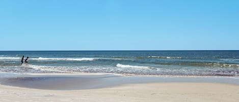 A beach with a clear sky, calm sea, and footprints in the sand.