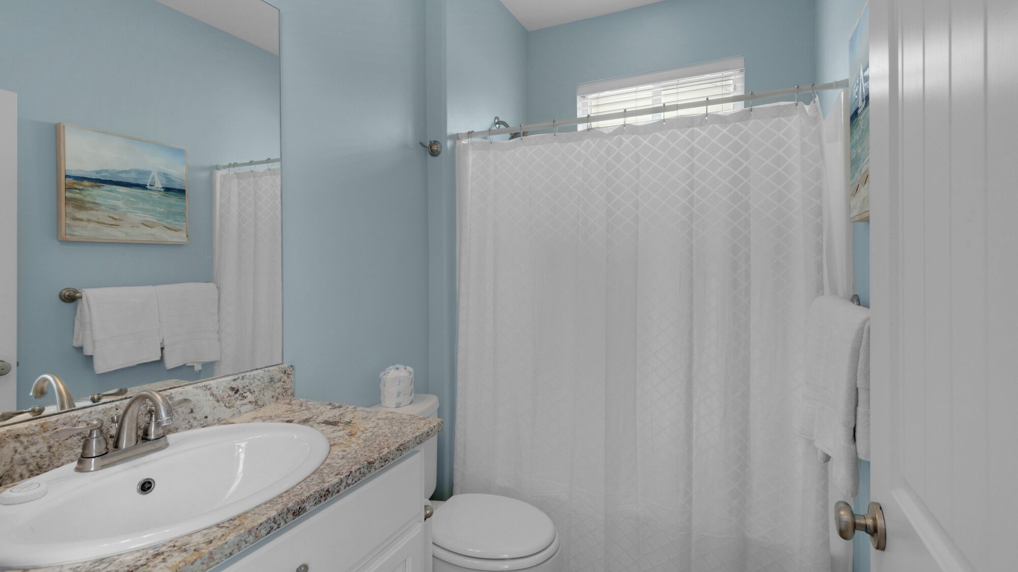 A bathroom with a white sink, a mirror, a toilet, and a shower curtain.