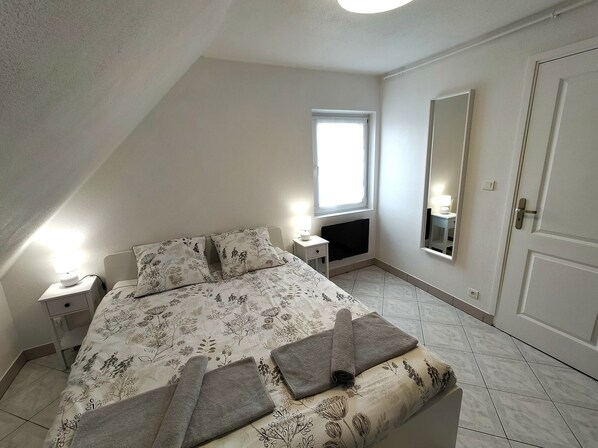 A bedroom with a bed, a nightstand, a window, a mirror, and a door.