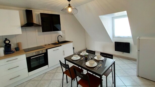 A modern kitchen with white cabinets, a black stove, and a dining table set for four. - Le 11 de Colmar (Colmar)