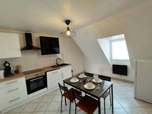 A modern kitchen with white cabinets, a black stove, and a dining table set for four.