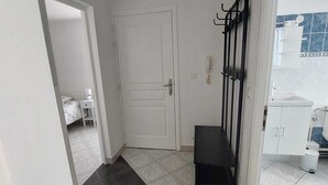 A hallway with a white door, a black bench, and a coat rack. - Le 11 de Colmar (Colmar)