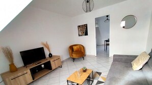 A modern living room with a sofa, a TV, a wooden cabinet, and a geometric patterned rug. - Le 11 de Colmar (Colmar)