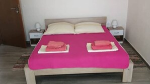 Un llit individual amb un edredó rosa, dos almoines i dues taules de nit amb làmpades.
