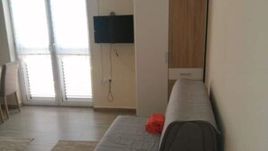 Una habitació amb un llit, una televisió penjada a la paret i una finestra corredissa amb sortida a un balcó.