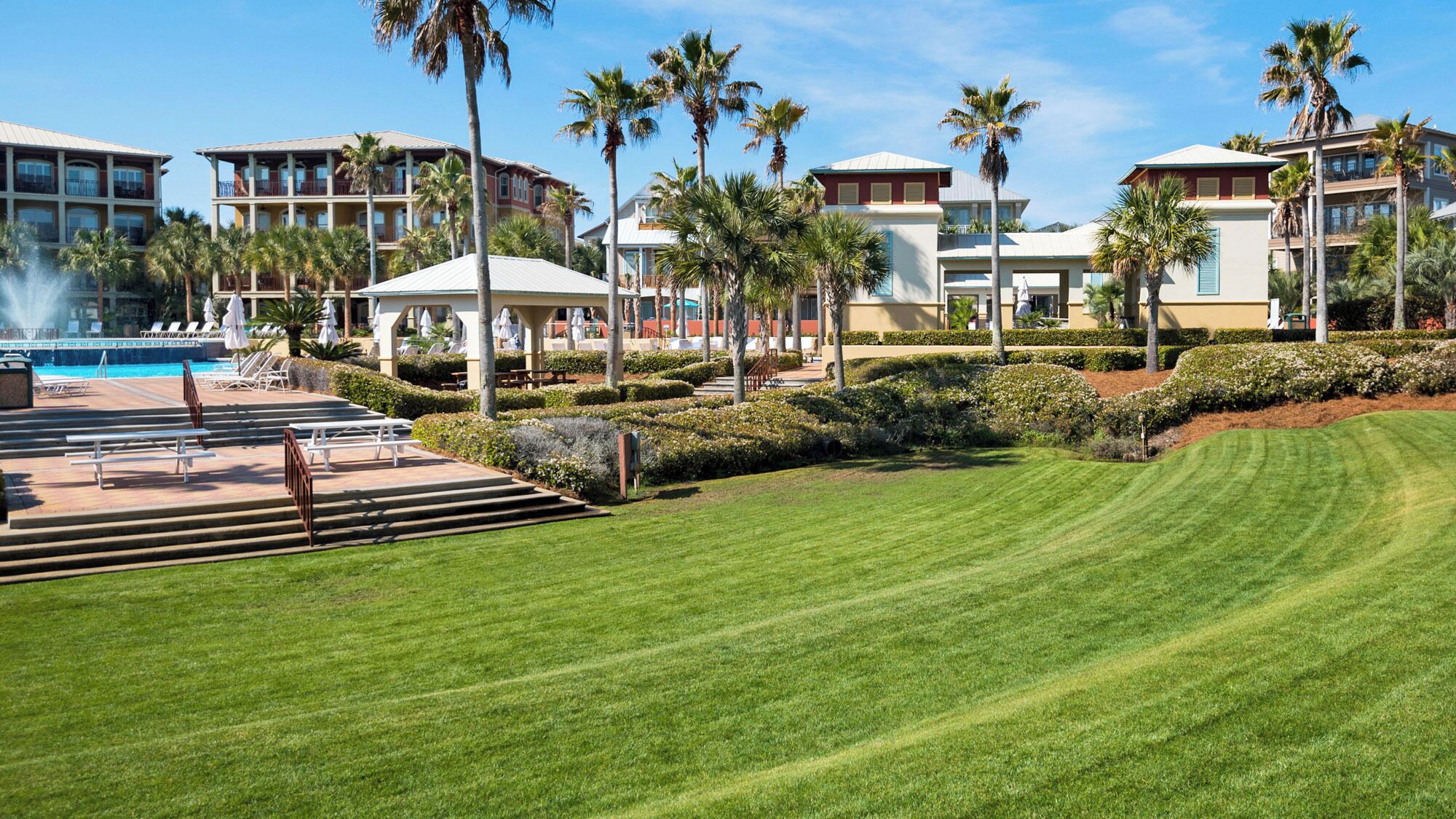 A resort with a swimming pool, palm trees, and a well-maintained lawn.